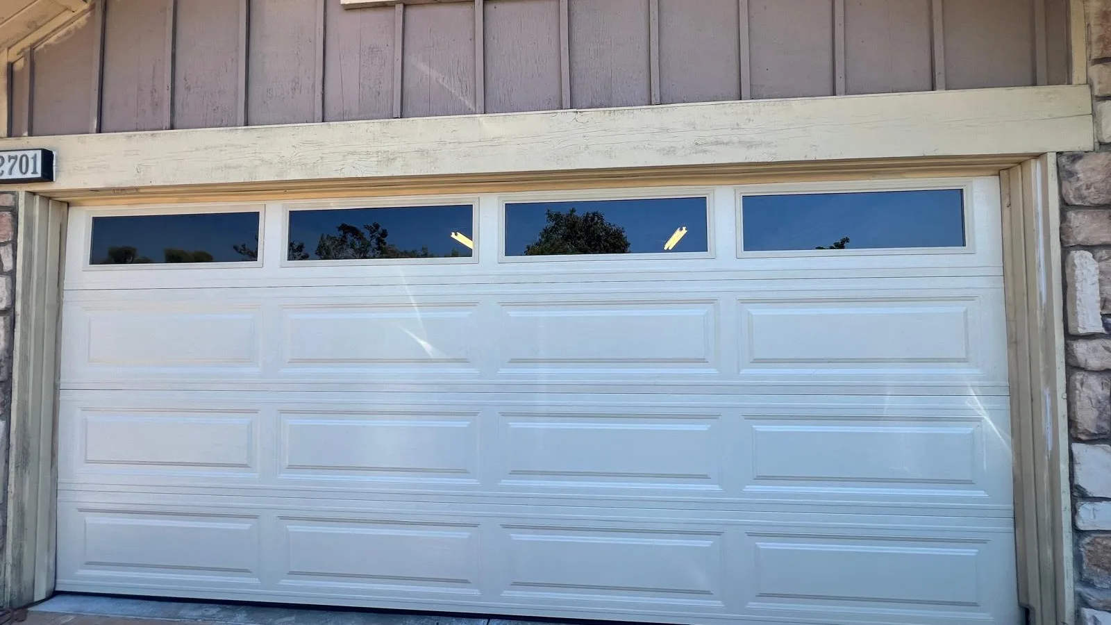 White raised-panel garage door with a row of four windows across the top, set in stone veneer